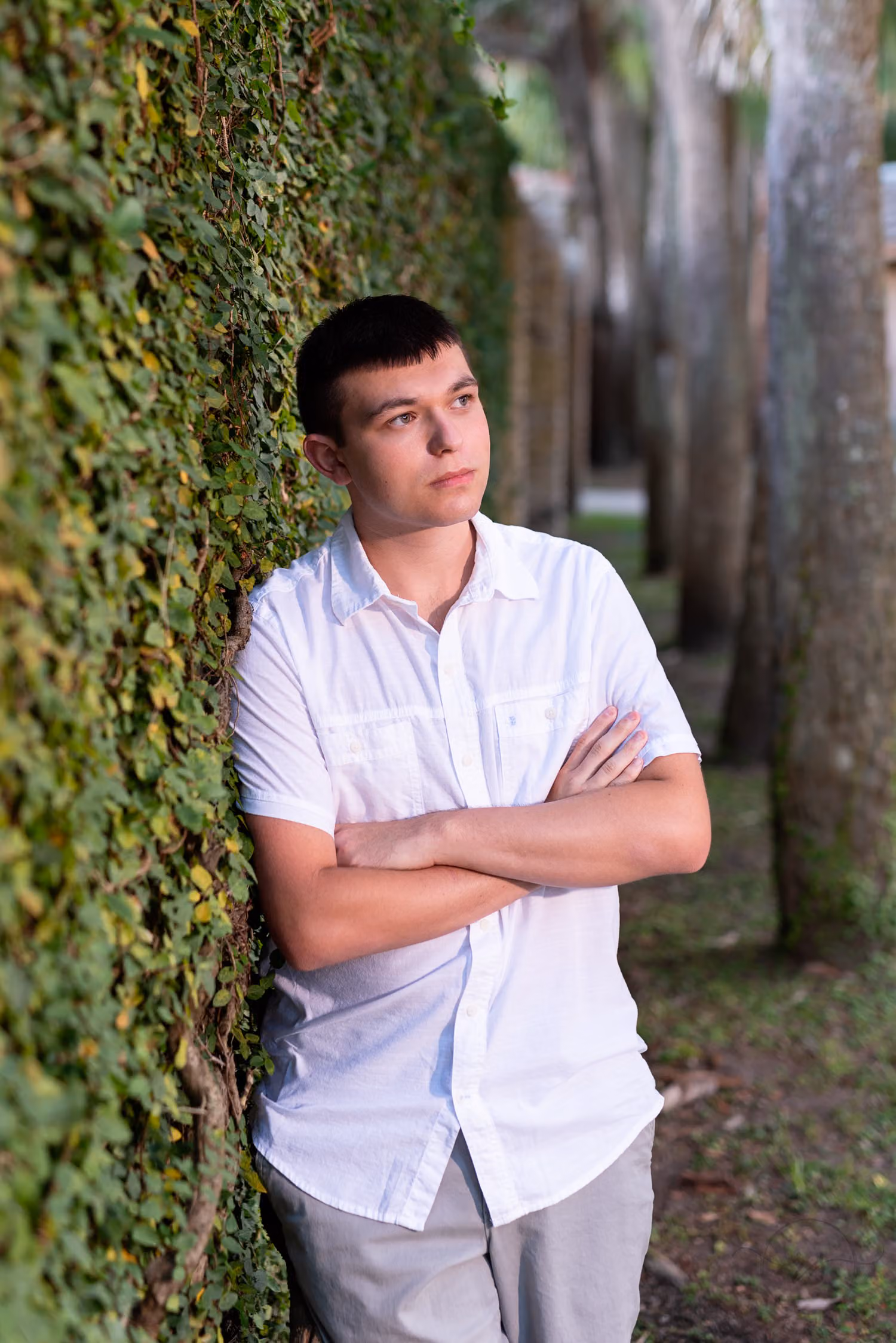 Senior guy in a white button-down with arms crossed, leaning on the ivy castle wall at Atalaya Castle