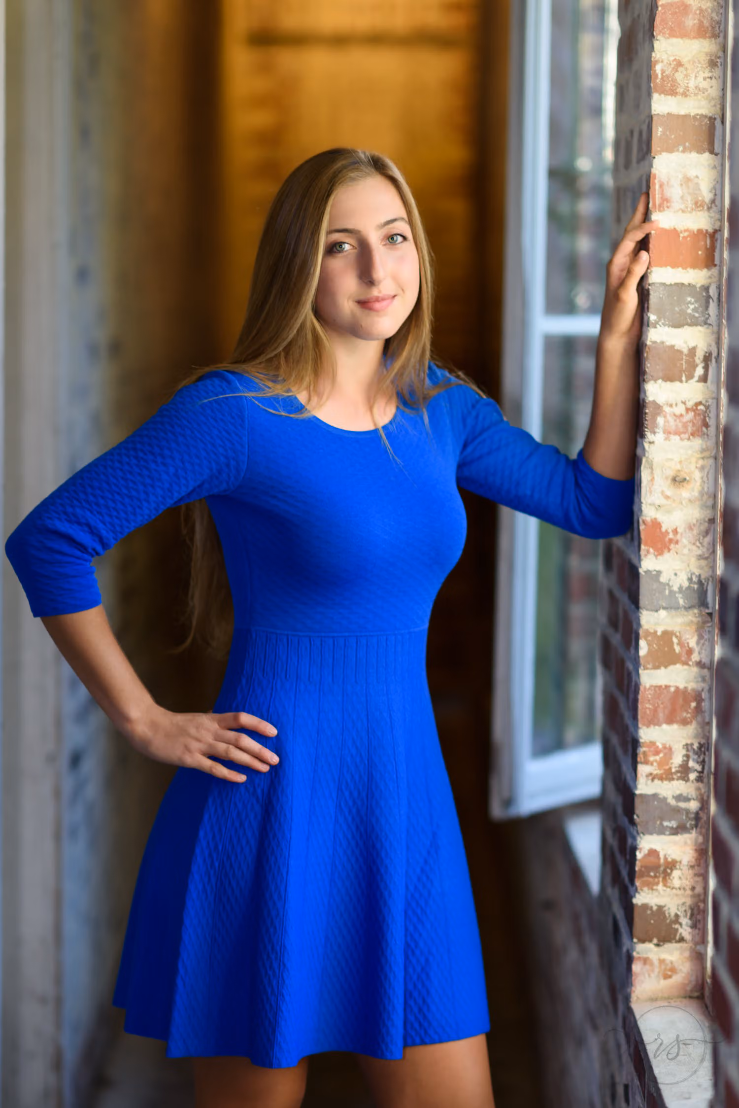 Senior in a royal blue dress standing in a doorway lit by soft window light at Atalaya Castle
