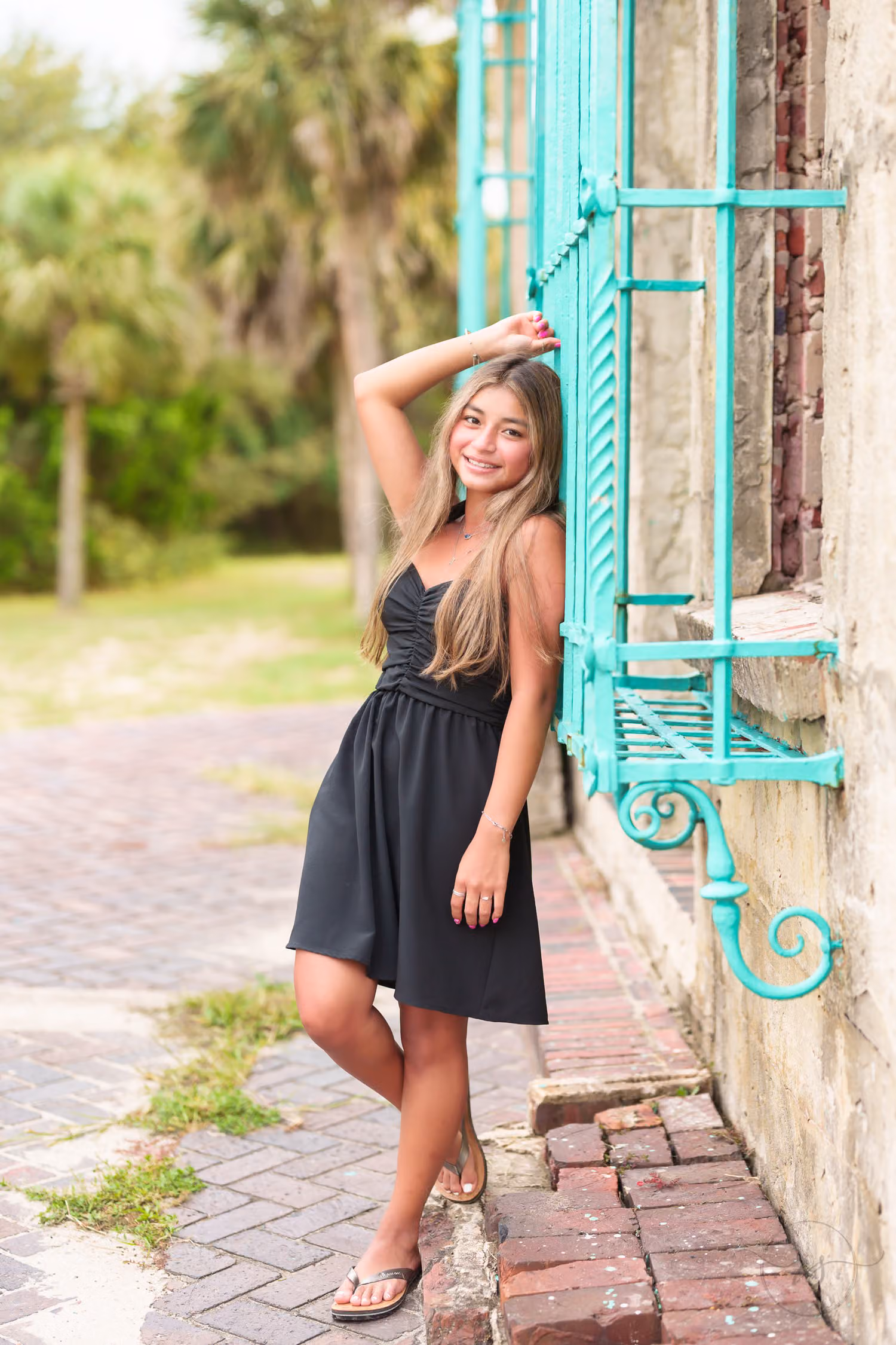 Senior in a black dress leaning against the green iron window grate on the castle wall at Atalaya Castle