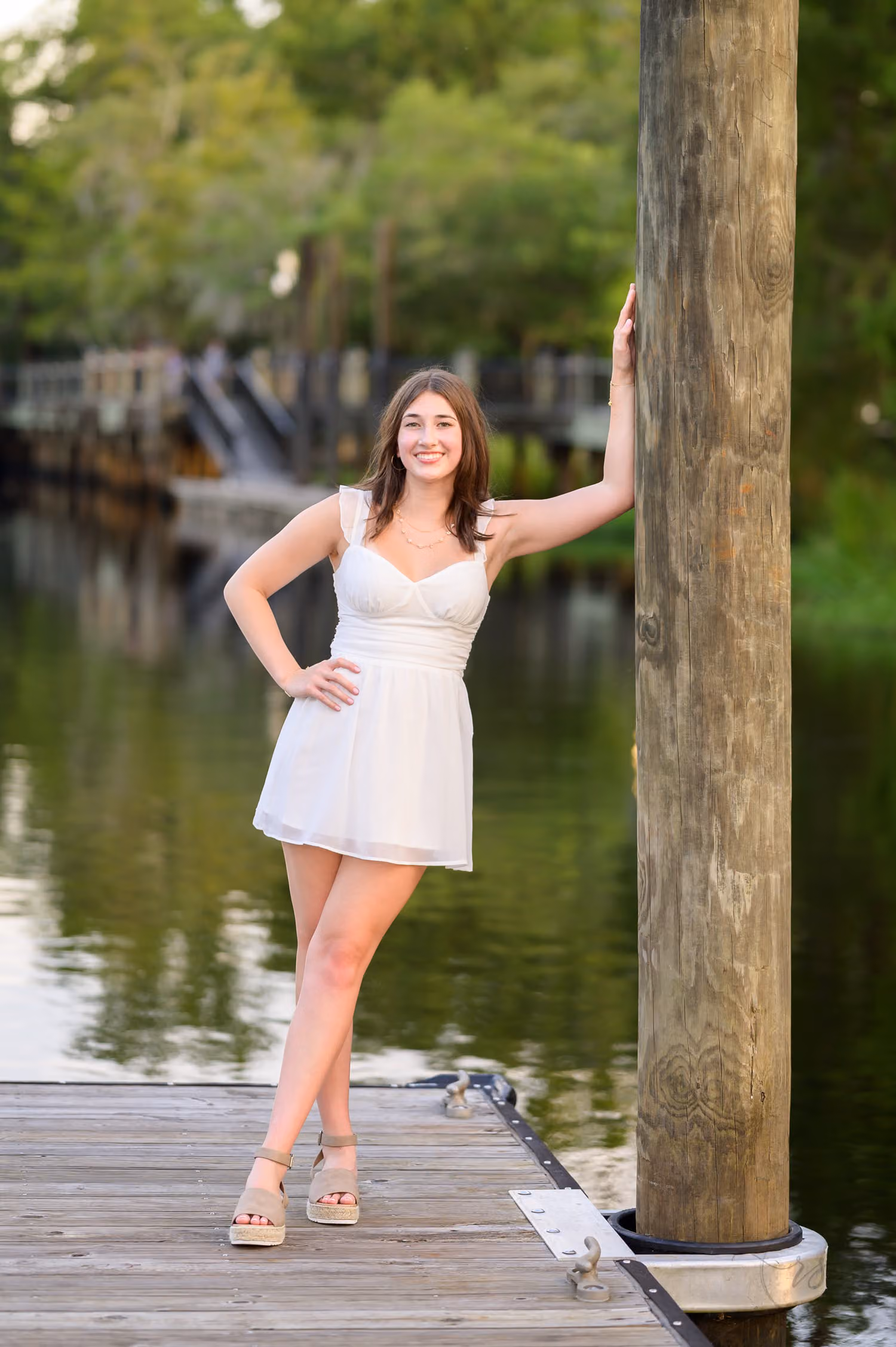 Senior girl in a white dress leaning on a dock piling over the river at the Conway River Walk