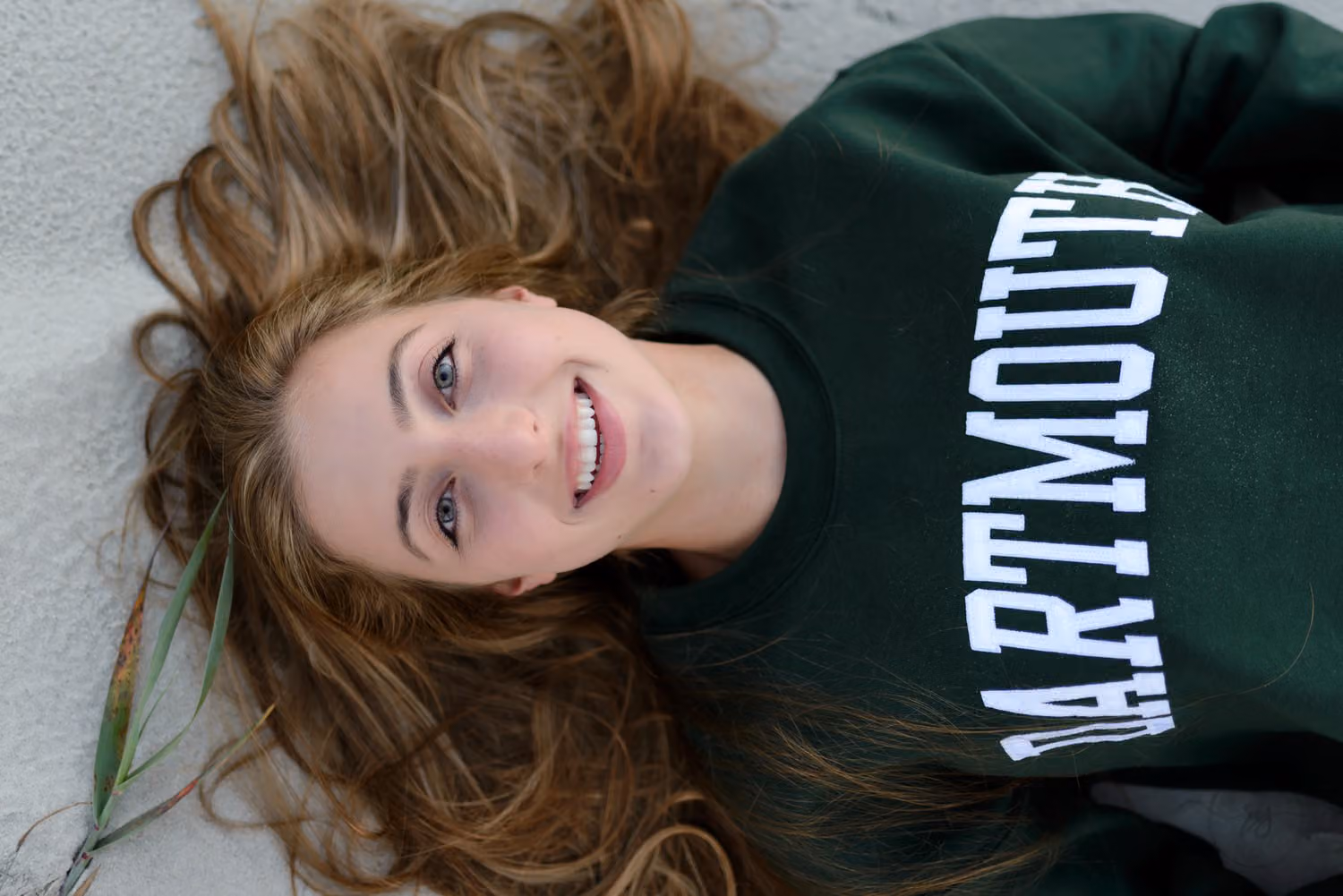 Close-up of a smiling senior lying back in the sand in a green college sweatshirt at Atalaya Castle