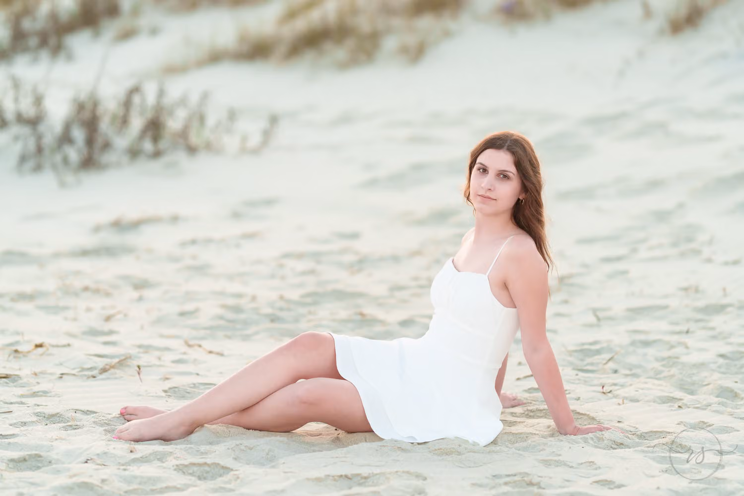 Senior girl in a white dress reclining in the sand by the dunes at Huntington Beach State Park