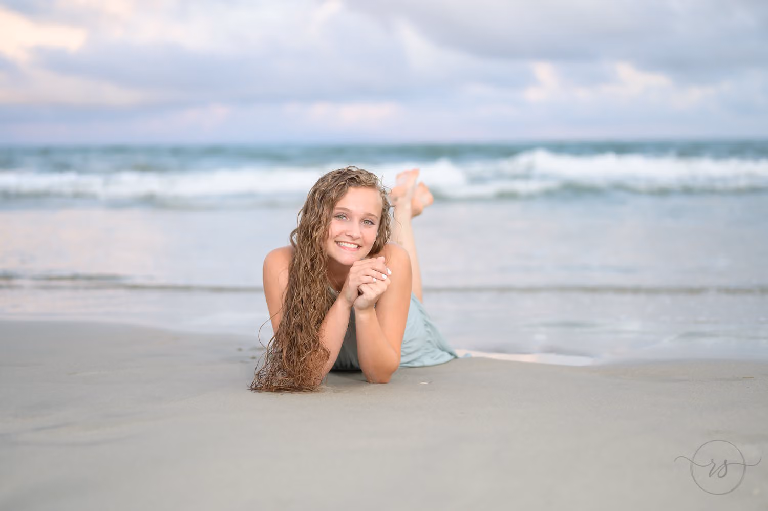 Senior girl lying on her stomach with her feet up at the edge of the ocean at Huntington Beach State Park