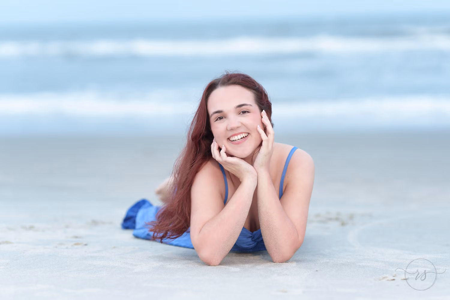 Smiling senior lying on the wet sand with her chin in her hands and the surf behind at Huntington Beach State Park