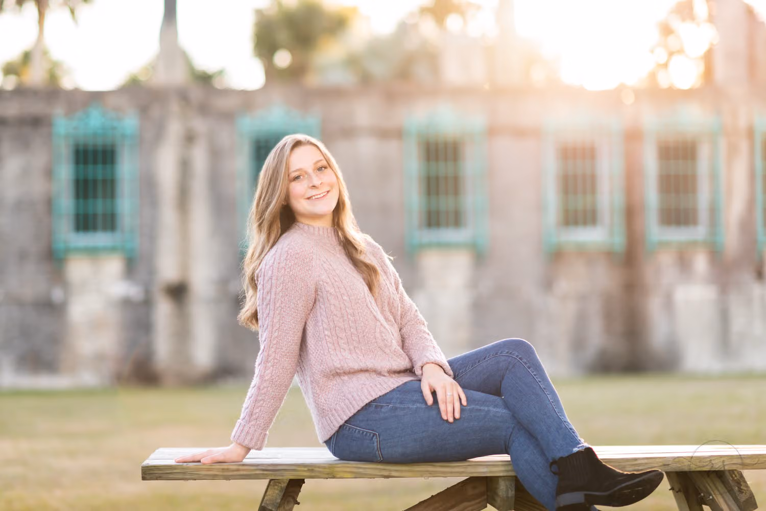 Senior in a pink sweater sitting on a picnic table in front of the castle at sunset at Atalaya Castle