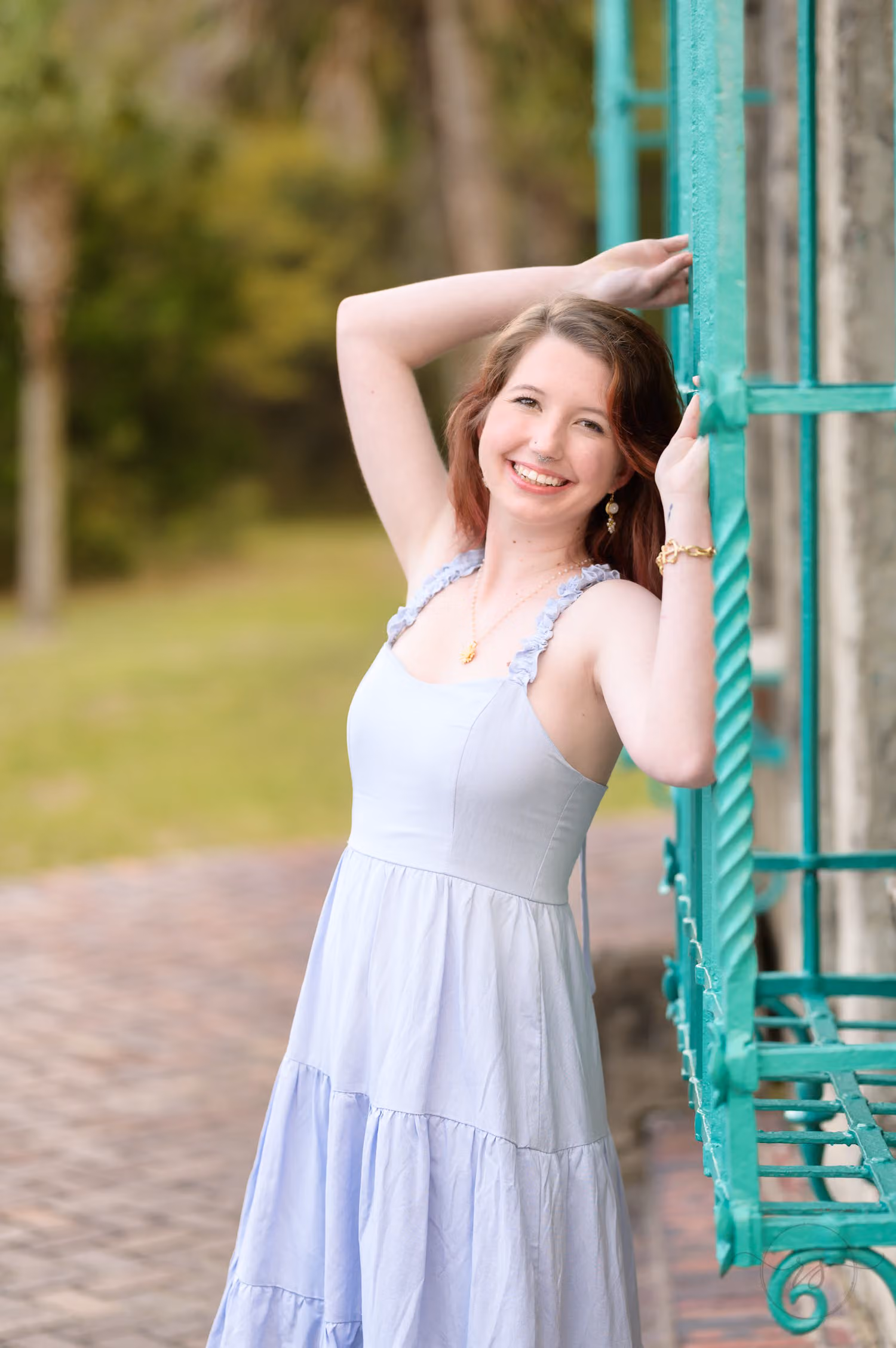 Senior girl in a light blue sundress posing with her arm raised beside a teal window grille at Atalaya Castle