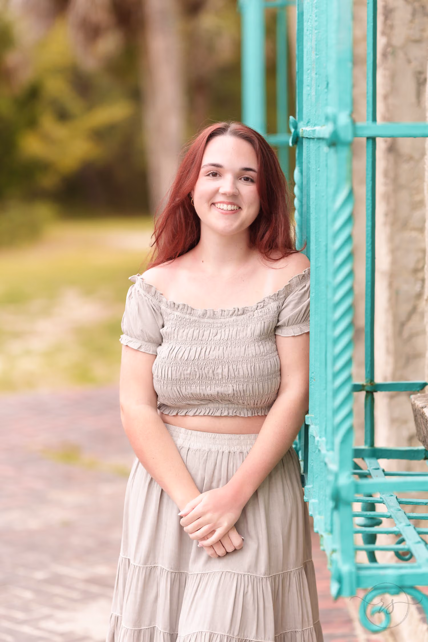 Red-haired senior in a taupe two-piece outfit smiling by the green iron window at Atalaya Castle
