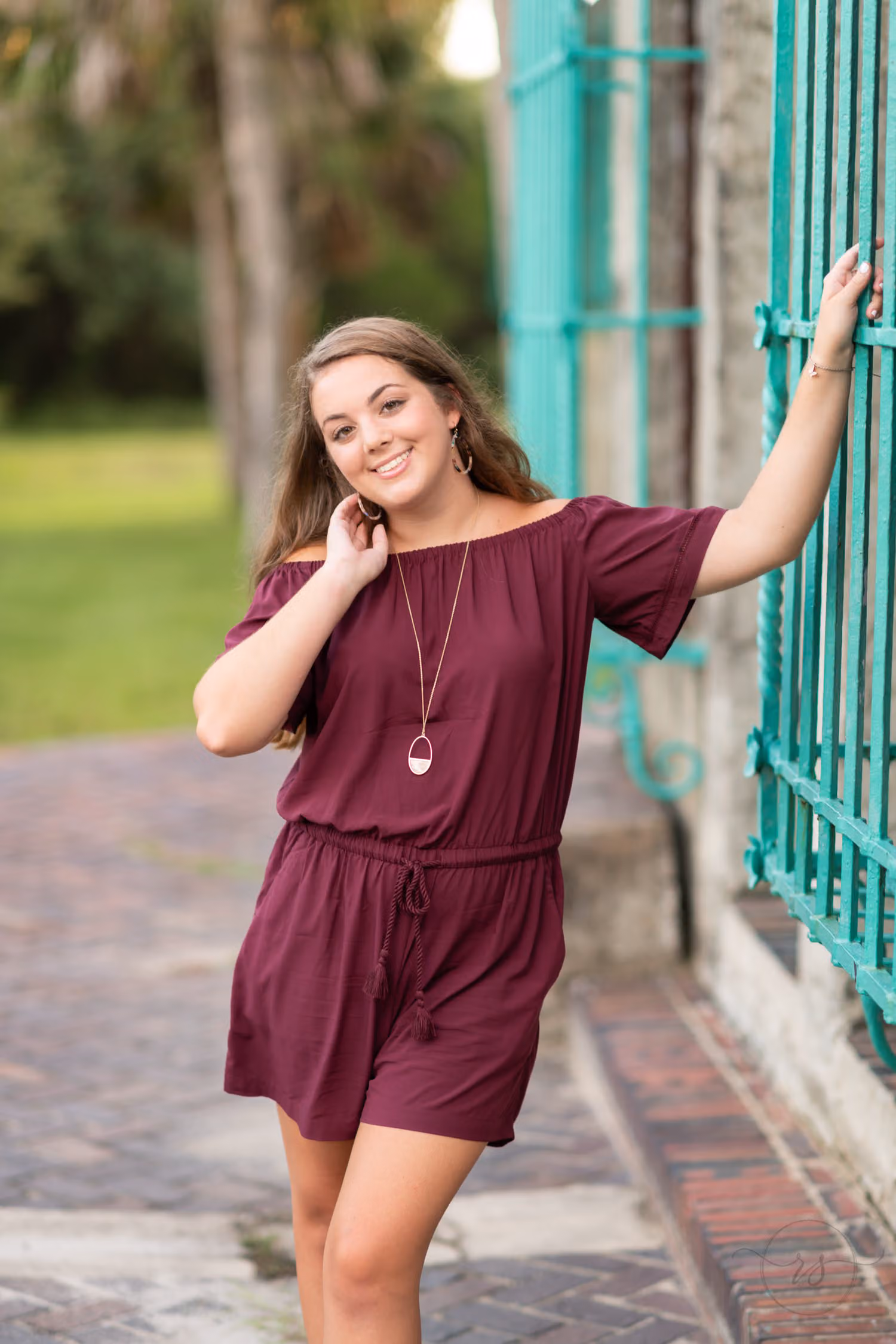Senior in a burgundy romper reaching up to the green wrought iron window grate at Atalaya Castle