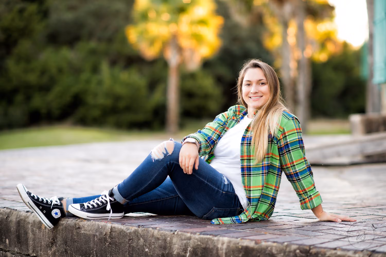 Senior in a plaid flannel and sneakers reclining on the low brick wall behind the castle at Atalaya Castle