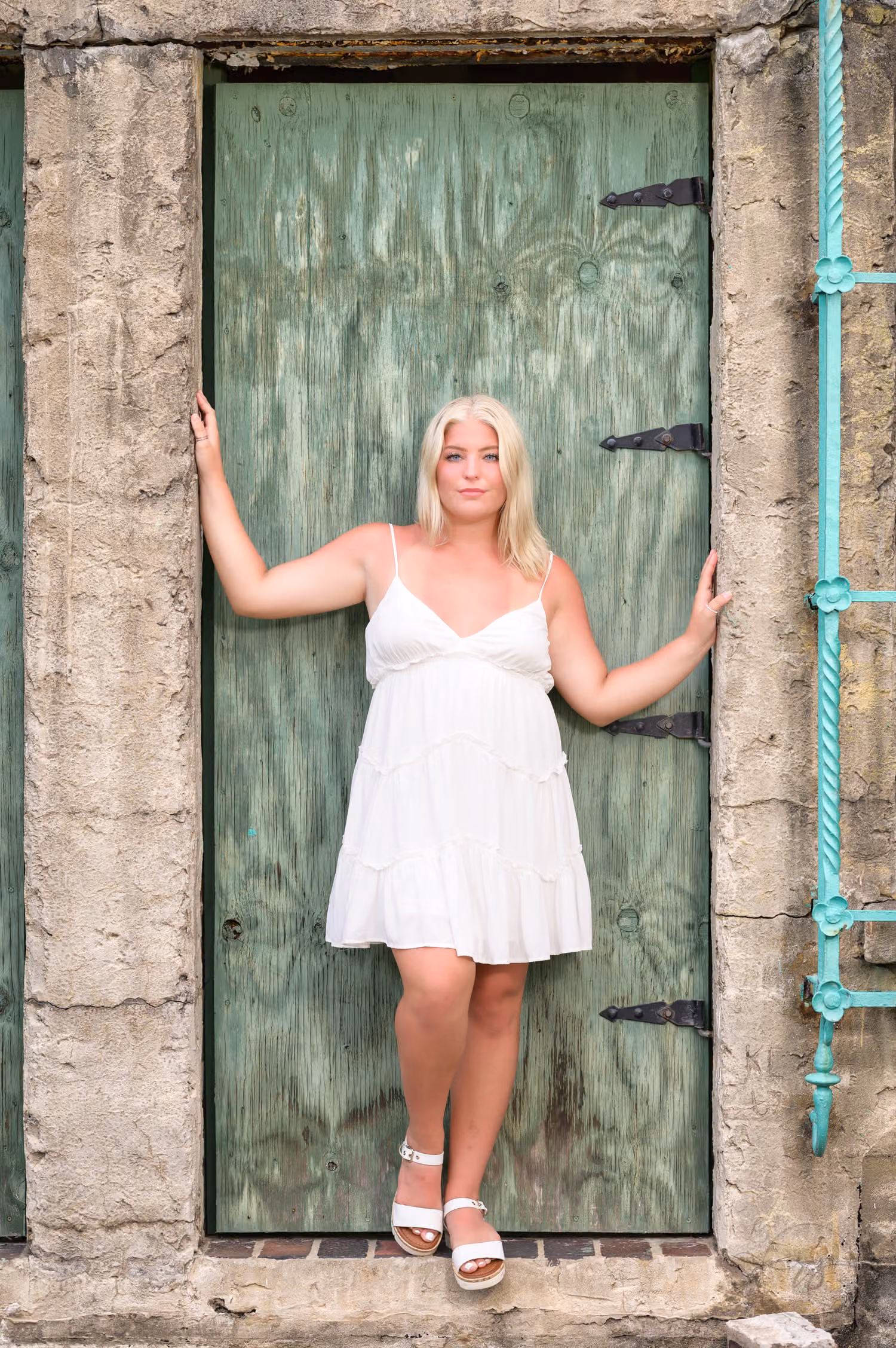 Senior in a white sundress with arms outstretched in the old green doorway at Atalaya Castle