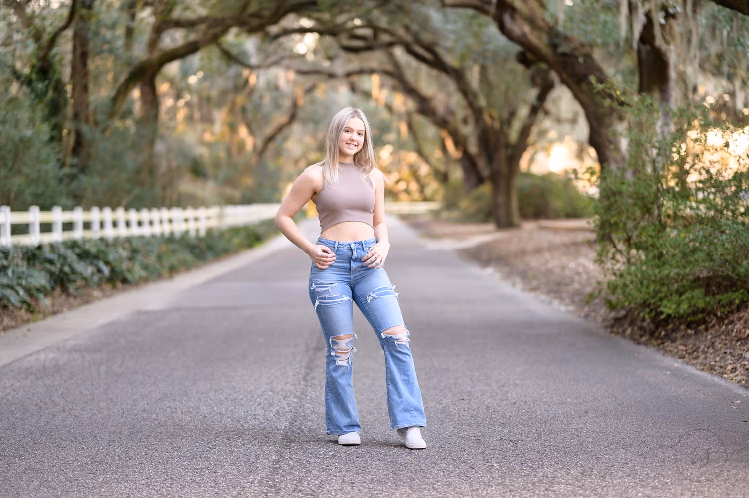 Senior girl in flared jeans standing on the road under an arch of moss-draped oaks at Caledonia Golf & Fish Club