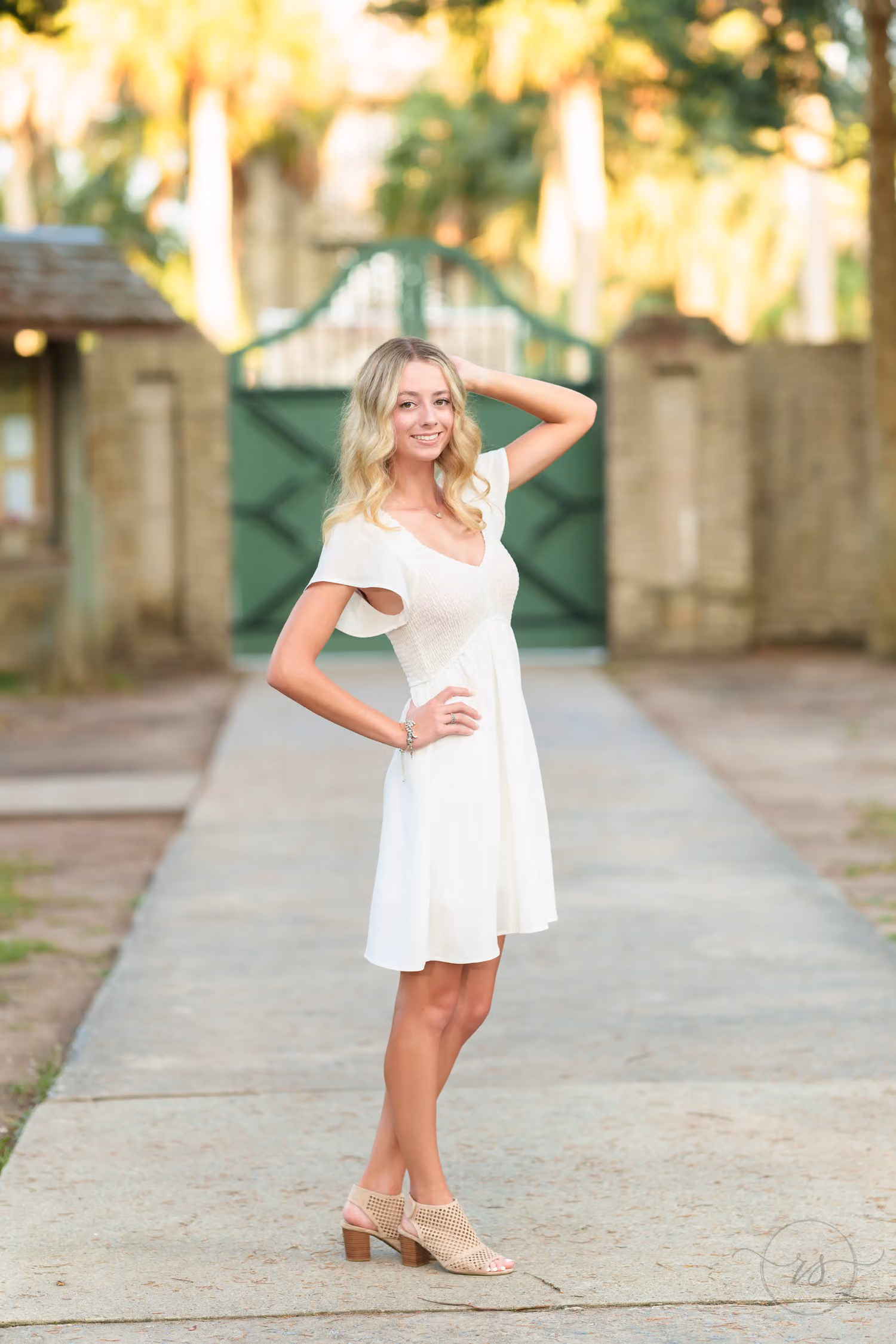 High school senior in a white dress with her hand in her hair on the walkway by the gate at Huntington Beach State Park
