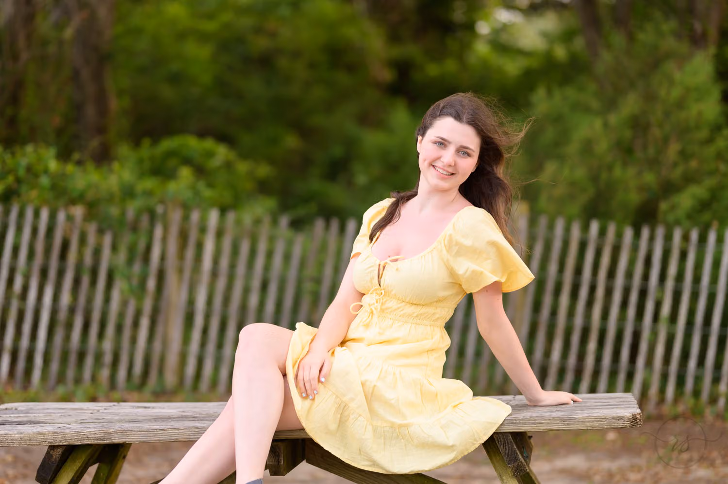 Senior in a yellow dress sitting on a picnic table beside a wooden fence at Myrtle Beach State Park