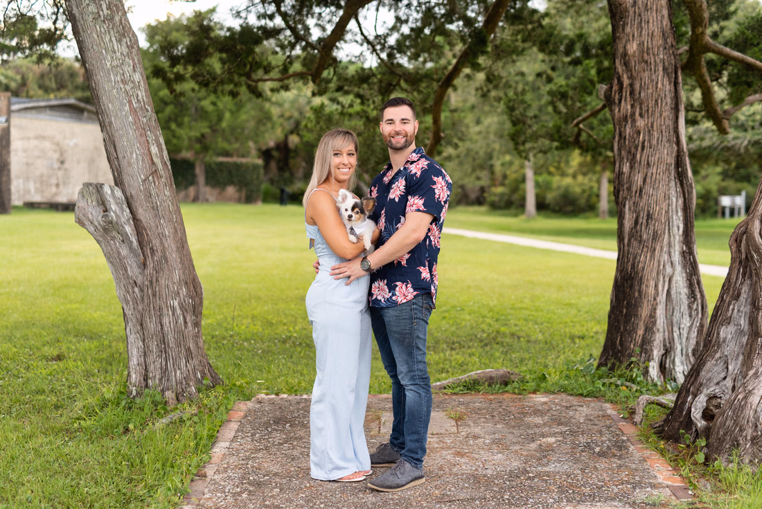Couple holding their small dog under the trees at Huntington Beach State Park