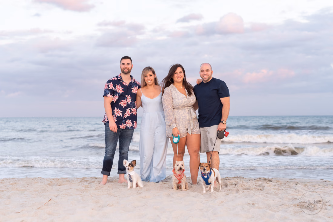 Two couples standing at the water's edge with their three small dogs at Huntington Beach State Park