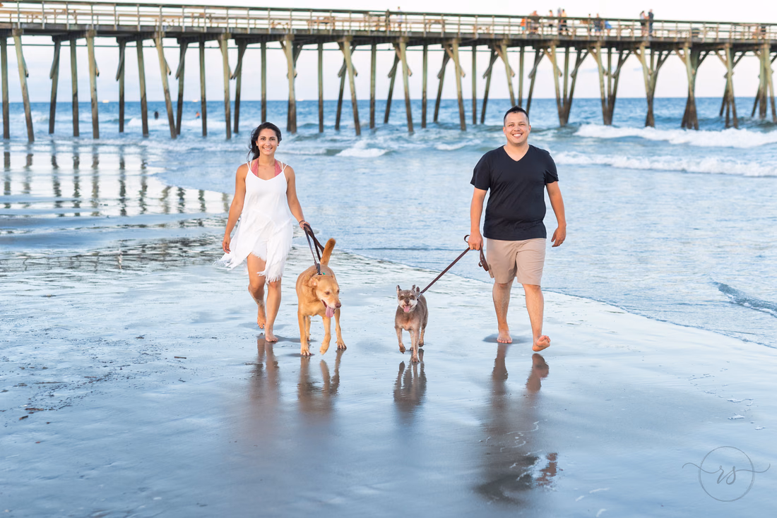 Couple walking their dogs on the beach by the pier at Myrtle Beach State Park