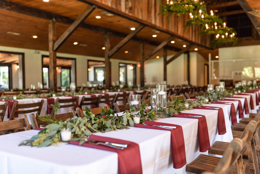 Long reception tables with burgundy napkins and greenery in the Carriage House at Magnolia Plantation