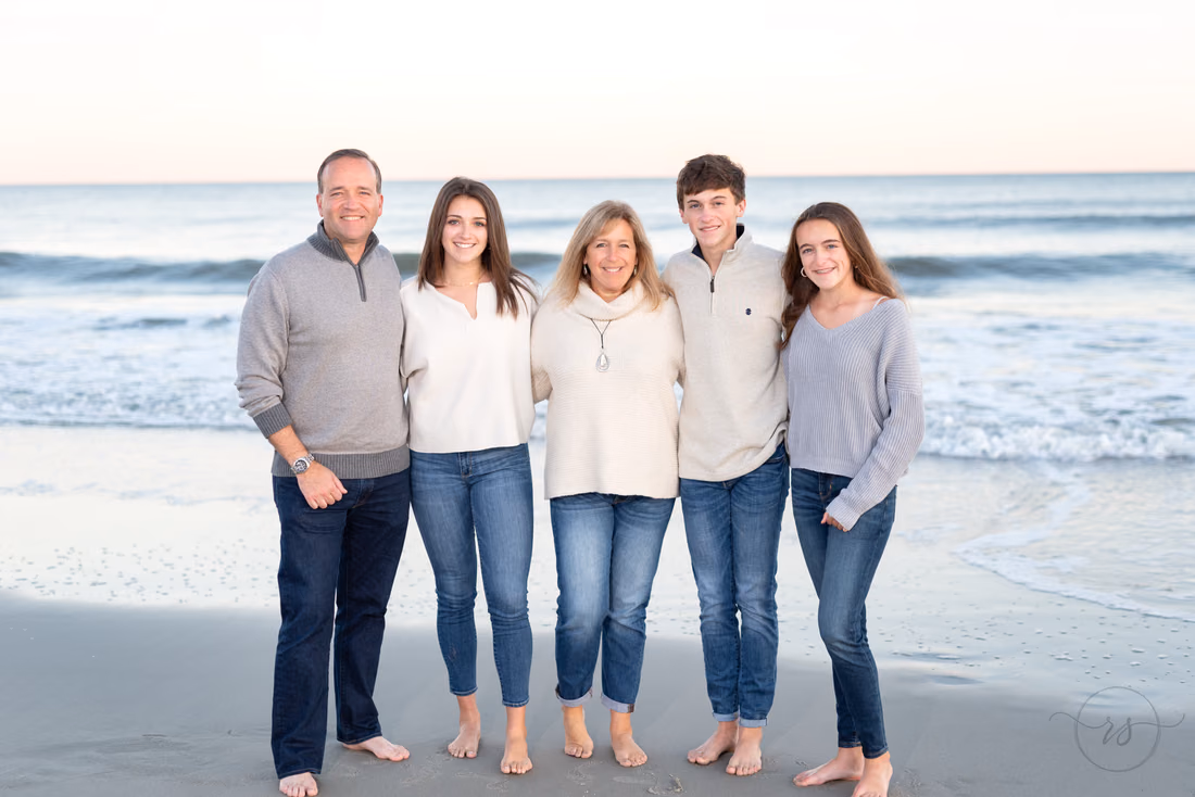 Family of five in cream and gray sweaters standing at the water's edge at Huntington Beach State Park