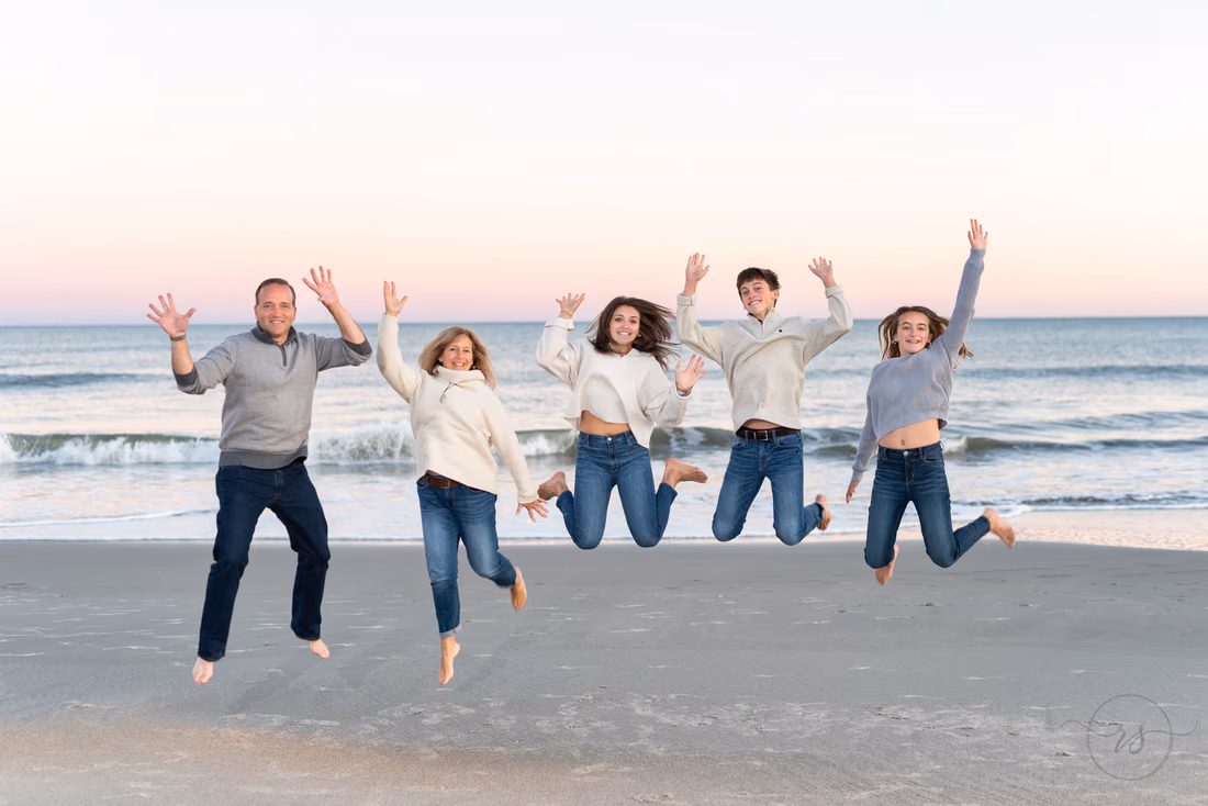 Family of five jumping in the air together on the beach at Huntington Beach State Park