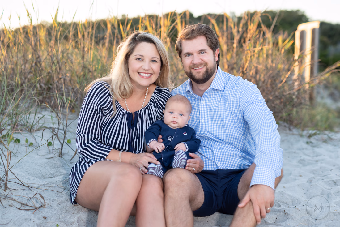 Parents sit in the sand in front of the sea oats with their baby boy at Huntington Beach State Park