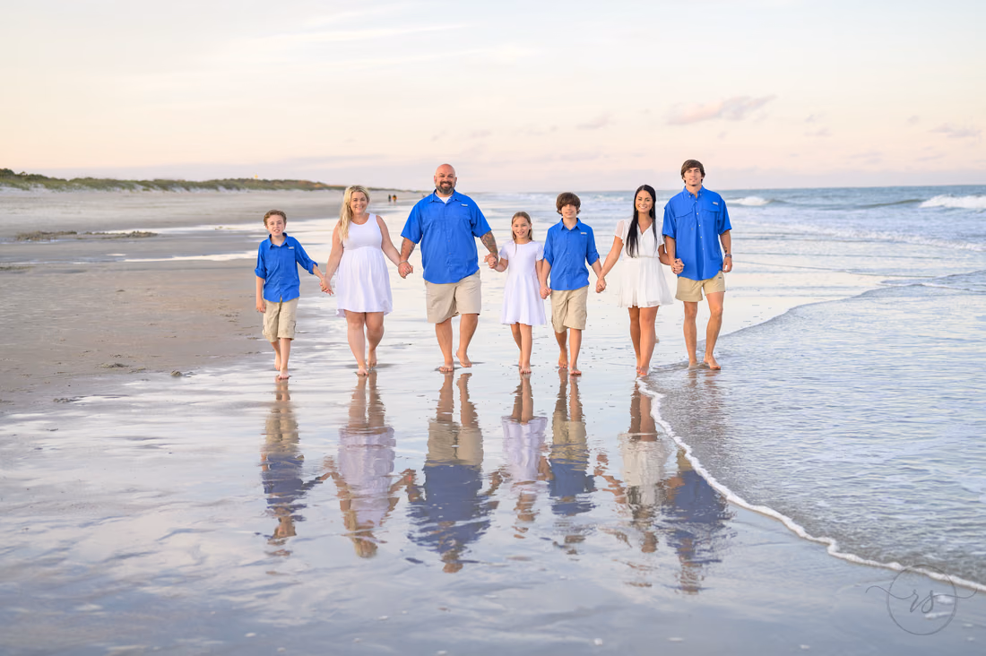 Family walks hand in hand through the shallow water at sunset at Huntington Beach State Park