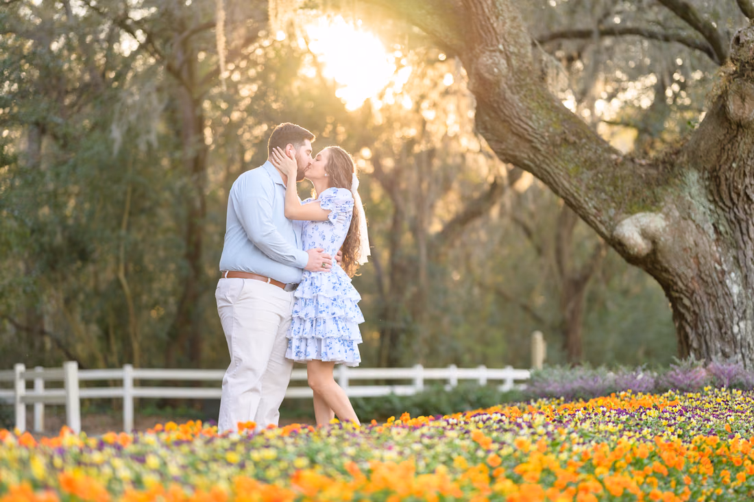Couple kissing by an orange and purple flower bed under a large oak at Caledonia Golf and Fish Club