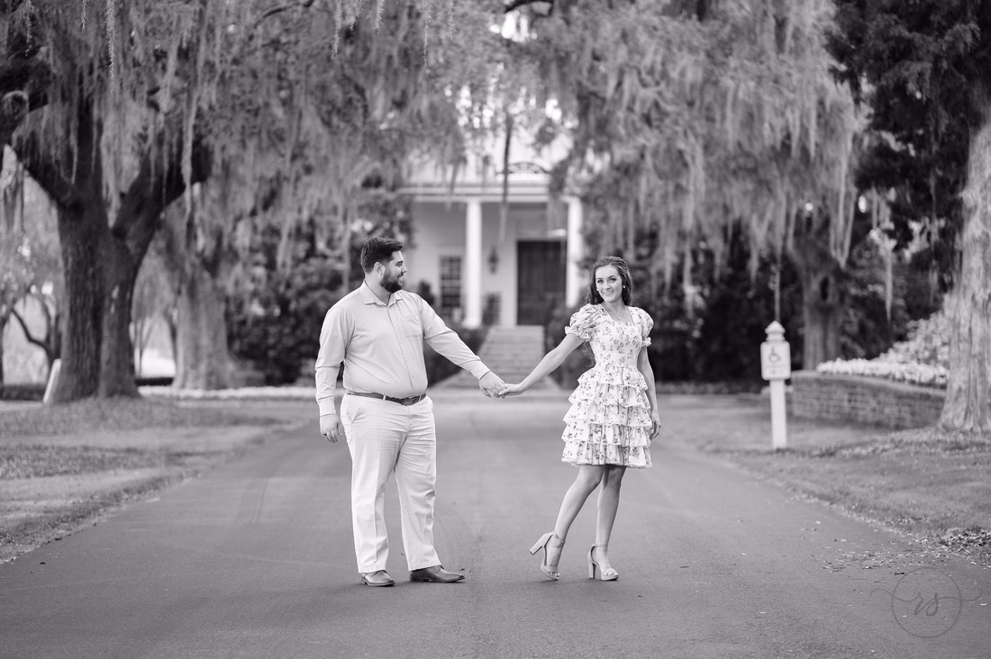 Black and white photo of the couple holding hands in front of the clubhouse at Caledonia Golf and Fish Club