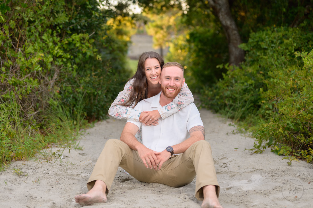 She hugs him from behind as they sit on the sandy beach path - Huntington Beach State Park
