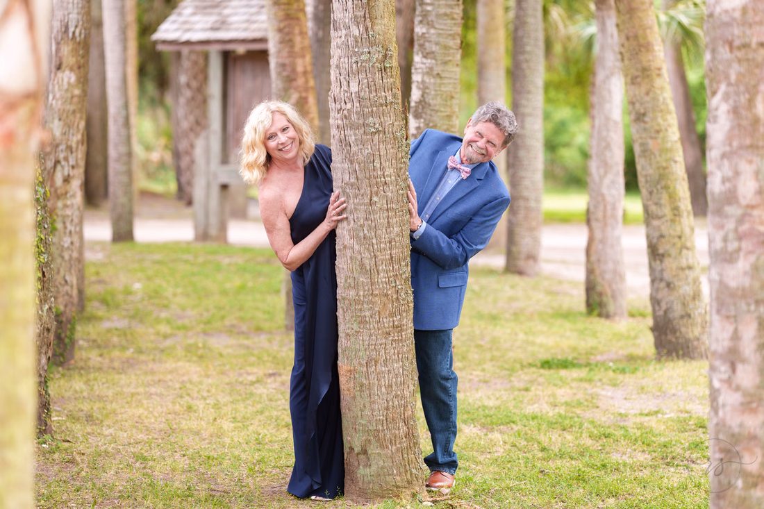 Happy senior couple peeking around the palm trees - Huntington Beach State Park