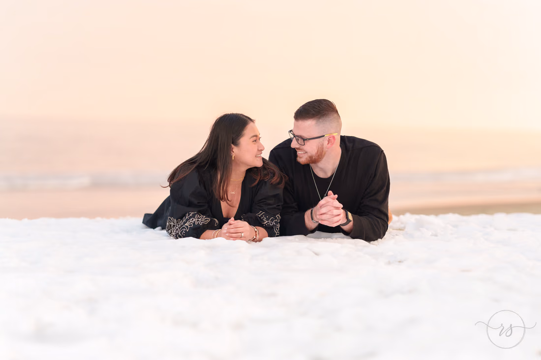 Couple lying in the snow smiling at each other - Garden City Beach