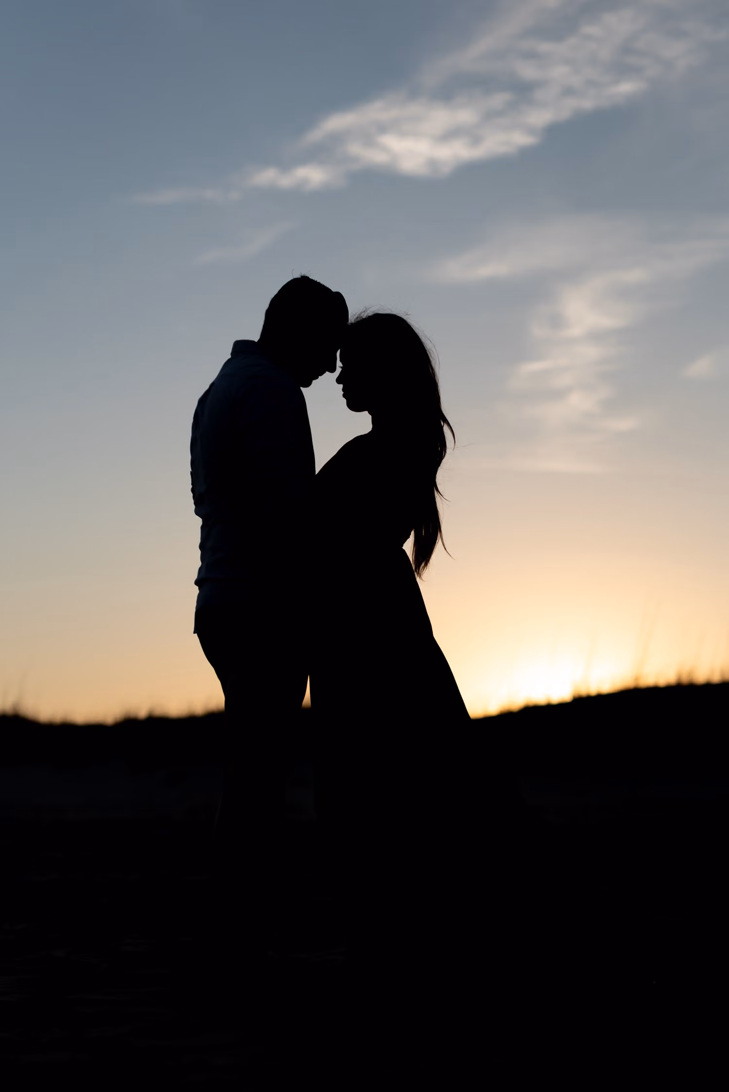 Silhouette of a couple touching foreheads against the evening sky as the sun sets at Huntington Beach State Park