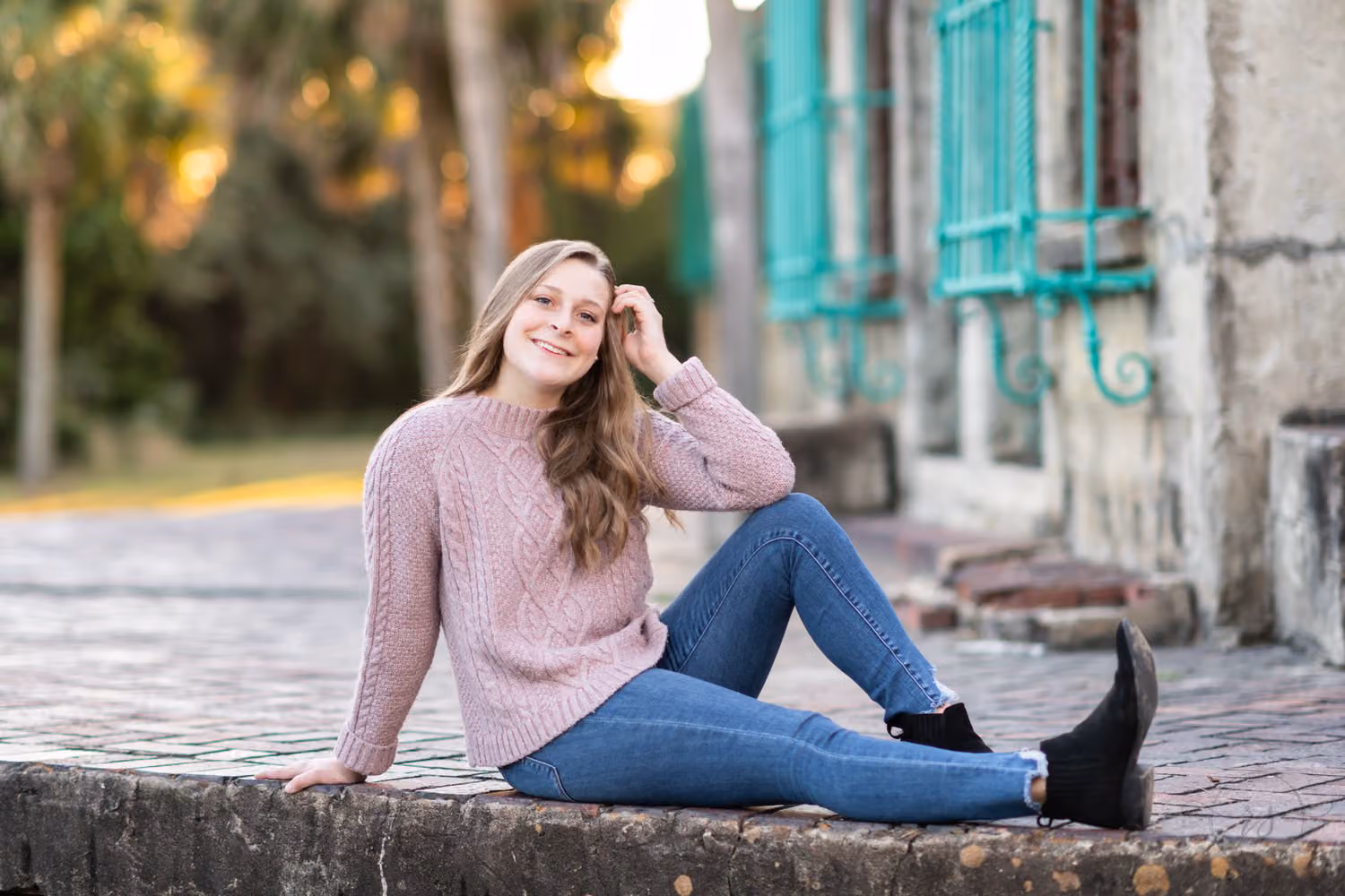 Senior in a pink sweater sitting on a brick ledge behind the castle with sunset light at Atalaya Castle