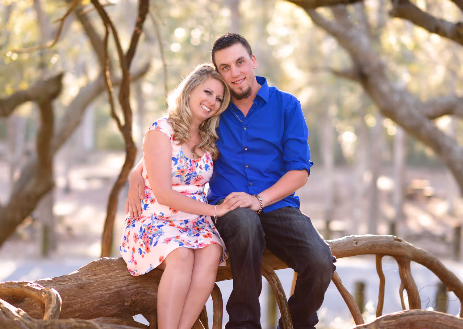 Couple sitting together on a low oak tree branch, she in a floral dress, at Myrtle Beach State Park