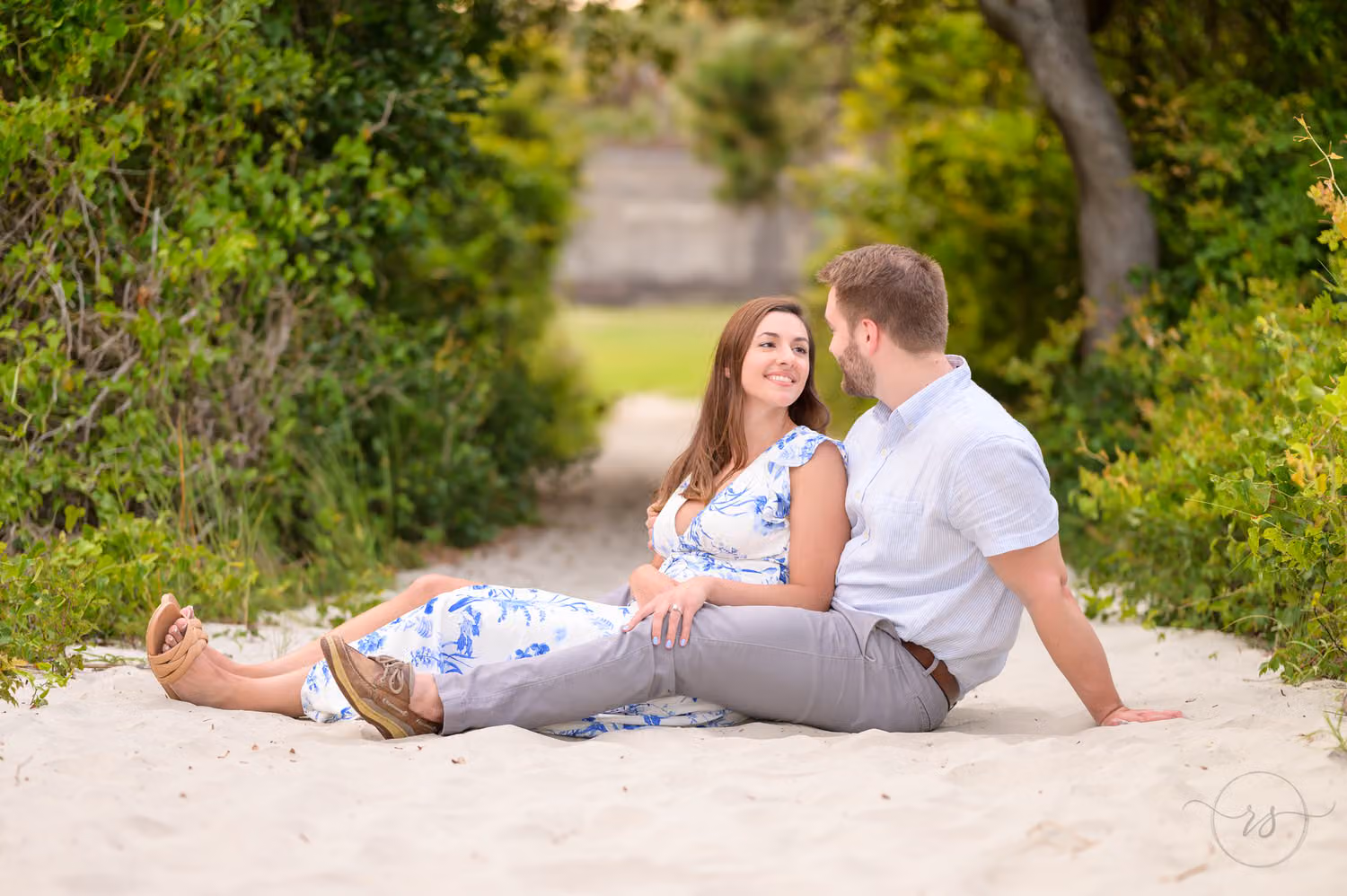 Couple in blue and white sitting close in the sand on a tree-lined beach path at Huntington Beach State Park