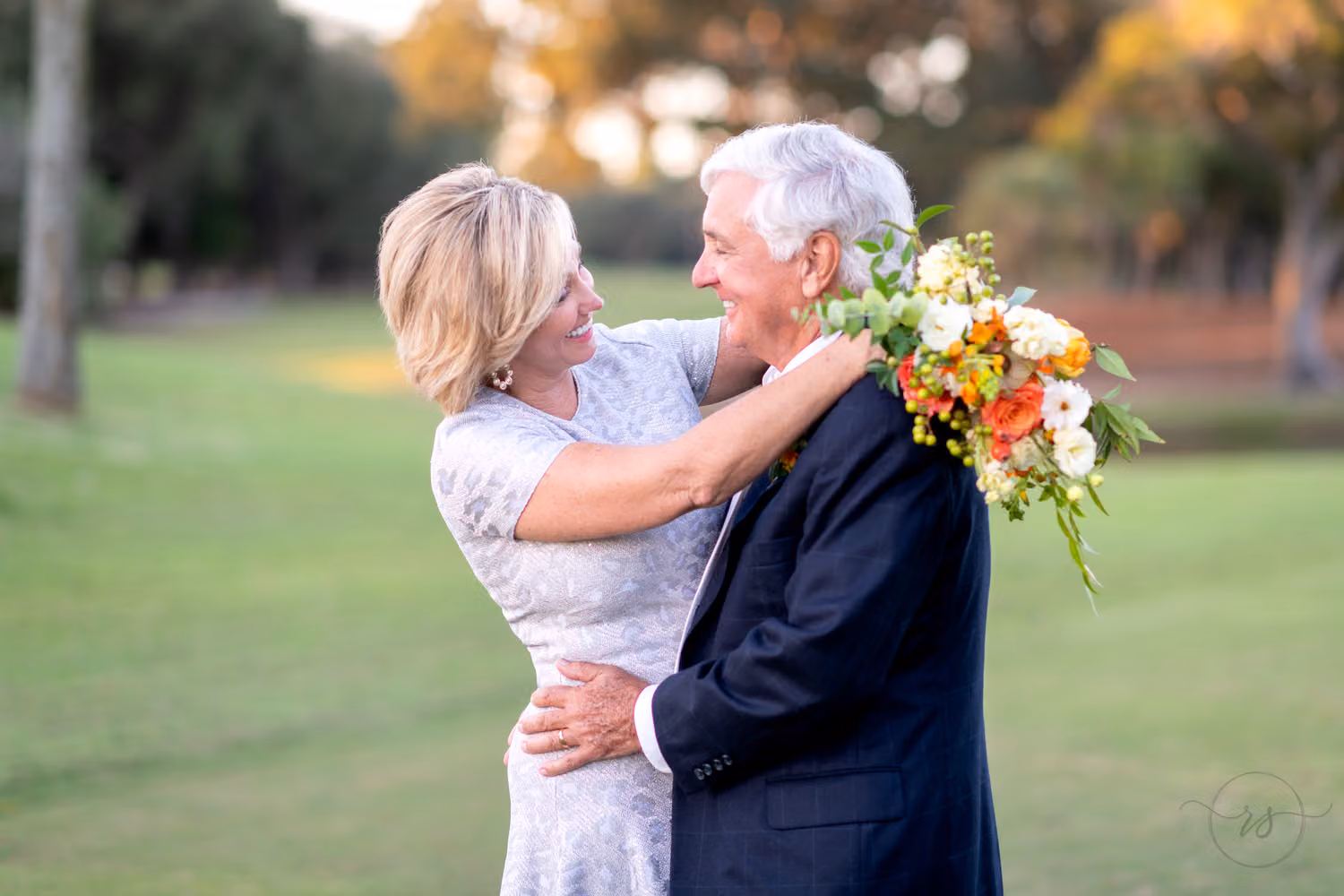 Bride with a bright bouquet and groom in navy smiling at each other on the golf course at Dunes Golf and Beach Club