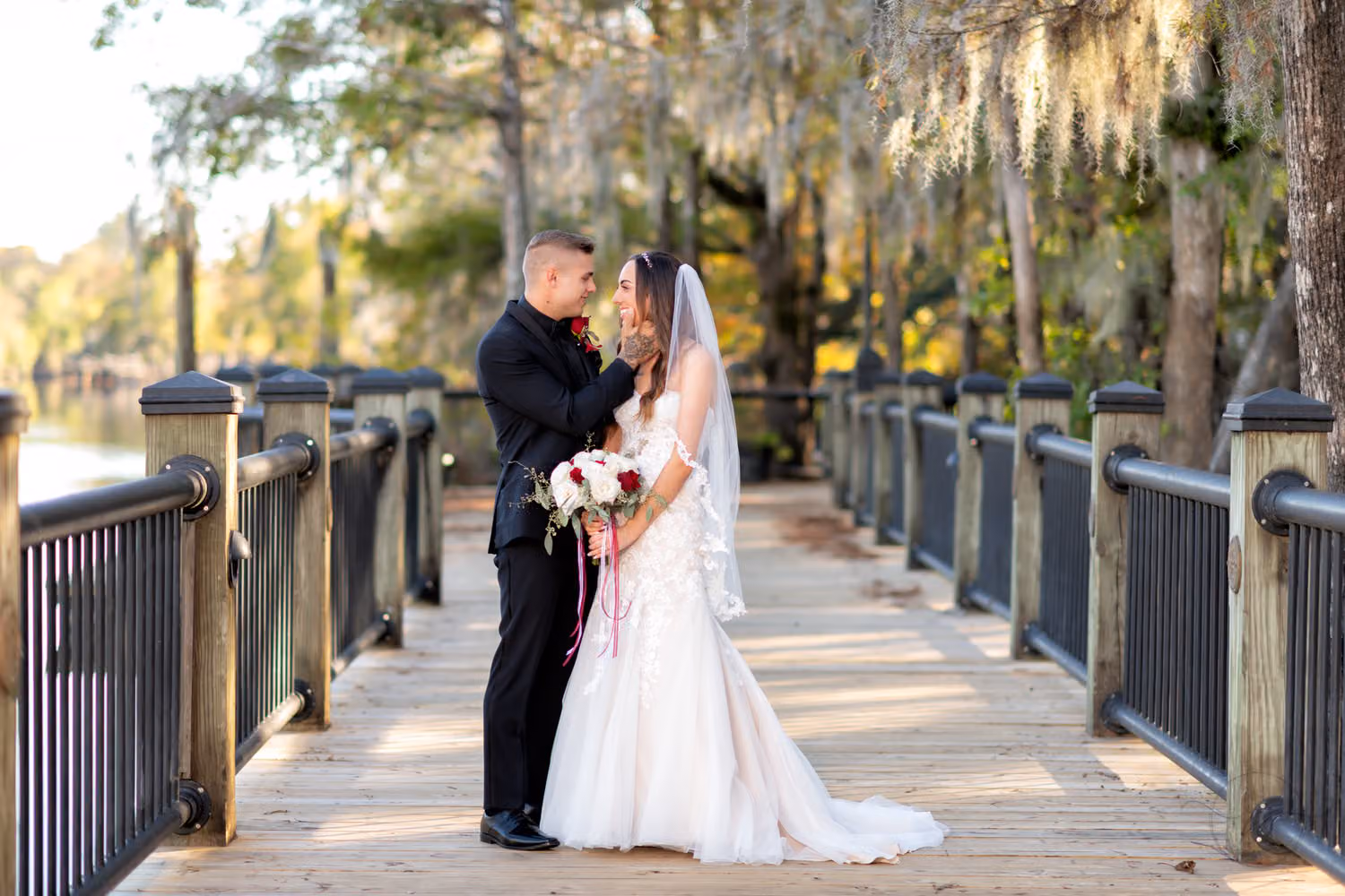 Bride and groom smiling at each other on a wooden boardwalk under moss-draped trees at the Conway Riverwalk