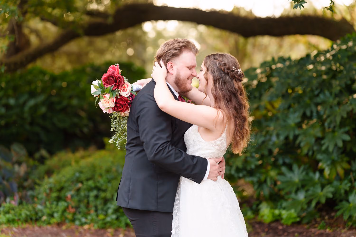 Bride and groom holding each other close under a sweeping oak limb in warm evening light at Litchfield Country Club