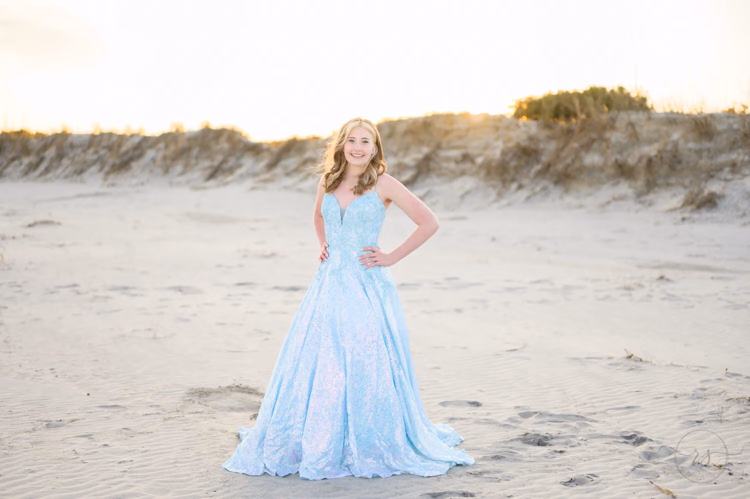Teen in a sparkly light blue prom gown standing on the sand in front of the dunes at Huntington Beach State Park