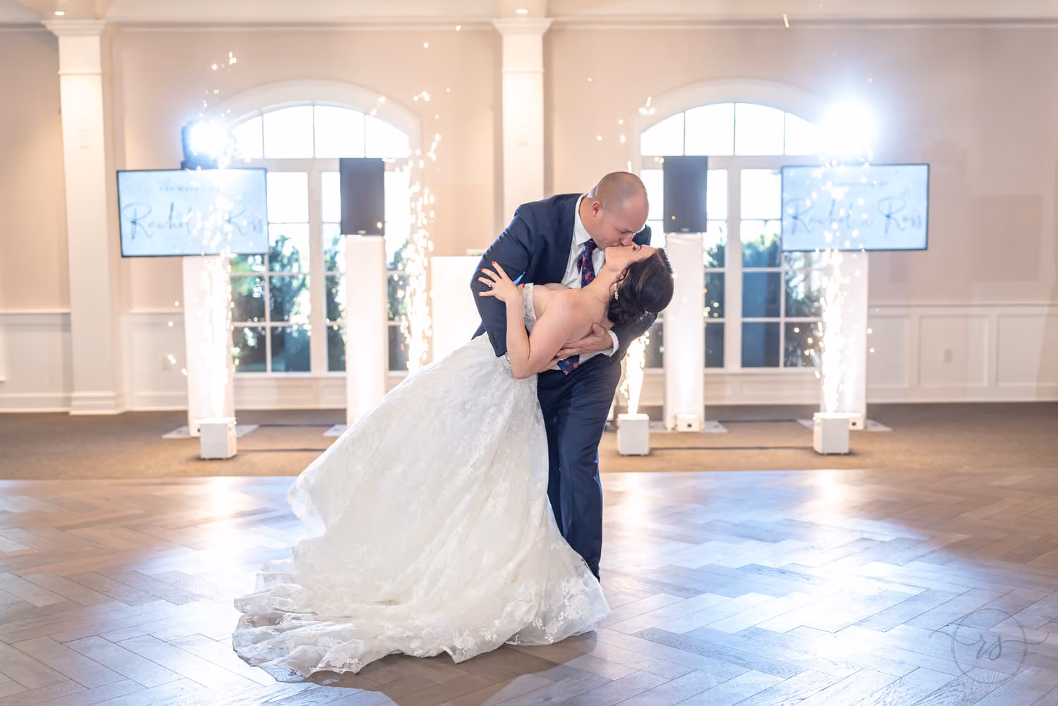 Groom dipping the bride for a kiss on the dance floor with cold spark fountains glowing behind them at 21 Main Events