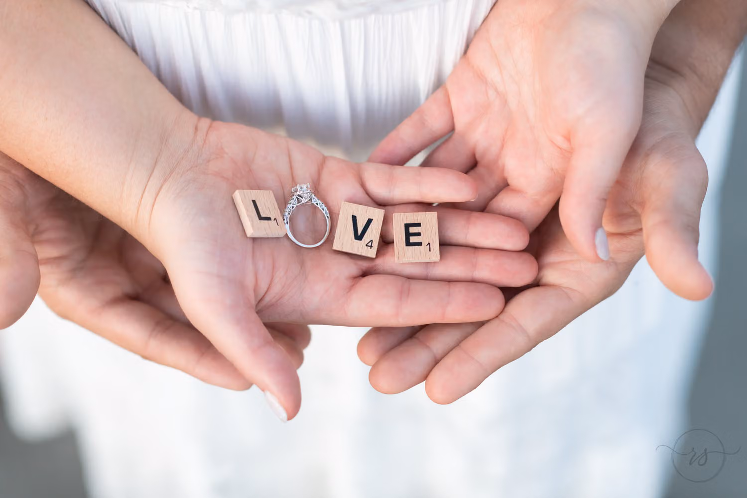 Cupped hands holding Scrabble tiles that spell love, with the engagement ring as the O, at Huntington Beach State Park