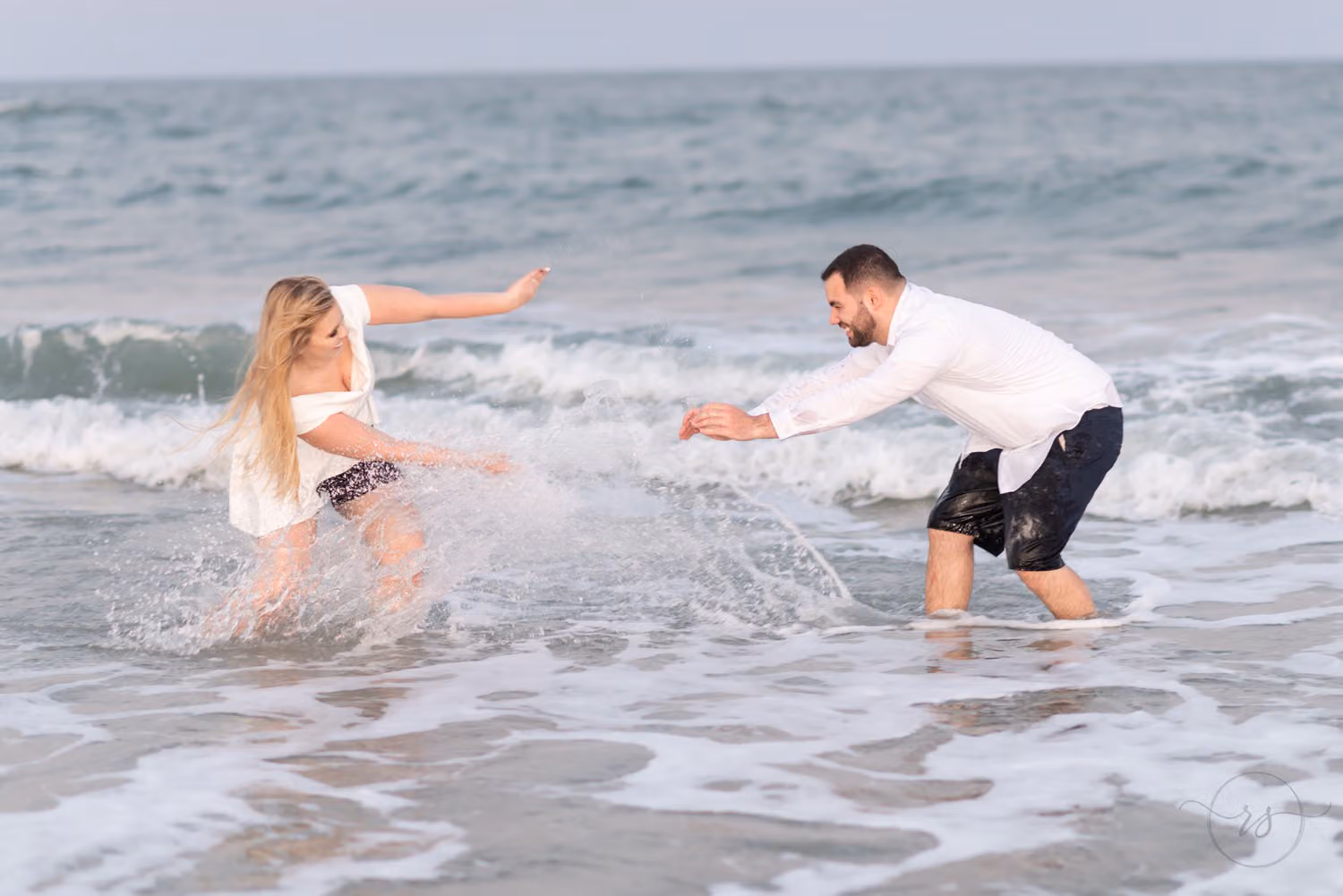 Couple splashing each other in the shallow waves, both laughing, at Huntington Beach State Park