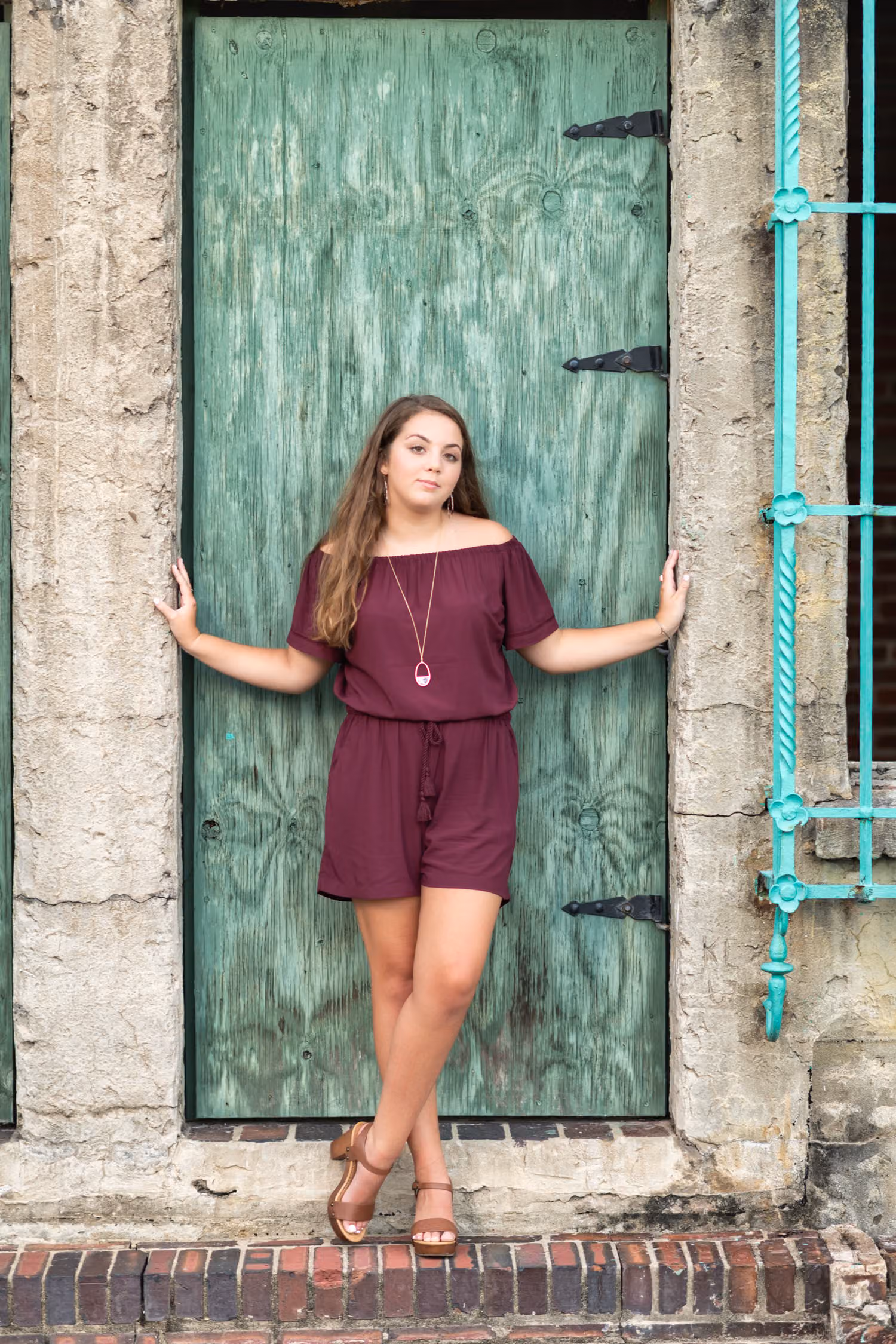 Senior in a burgundy romper standing with arms braced in the green castle doorway at Atalaya Castle
