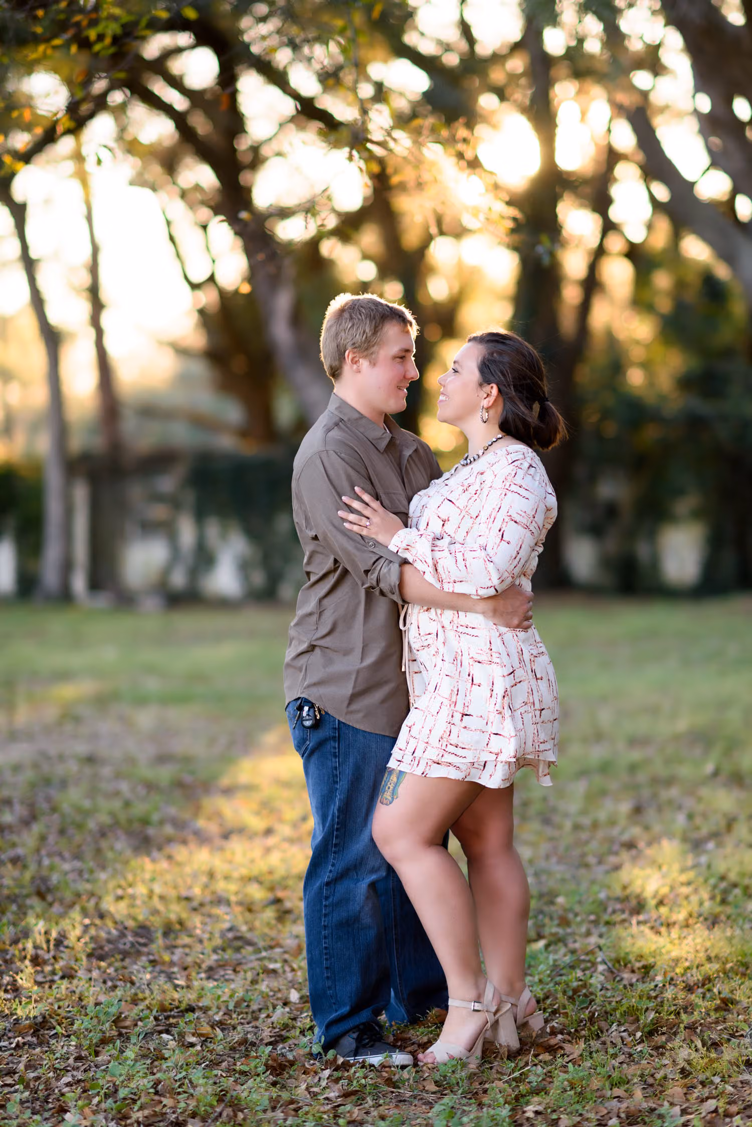 Couple holding each other on the grass as late sunlight shines through the trees in Pawleys Island