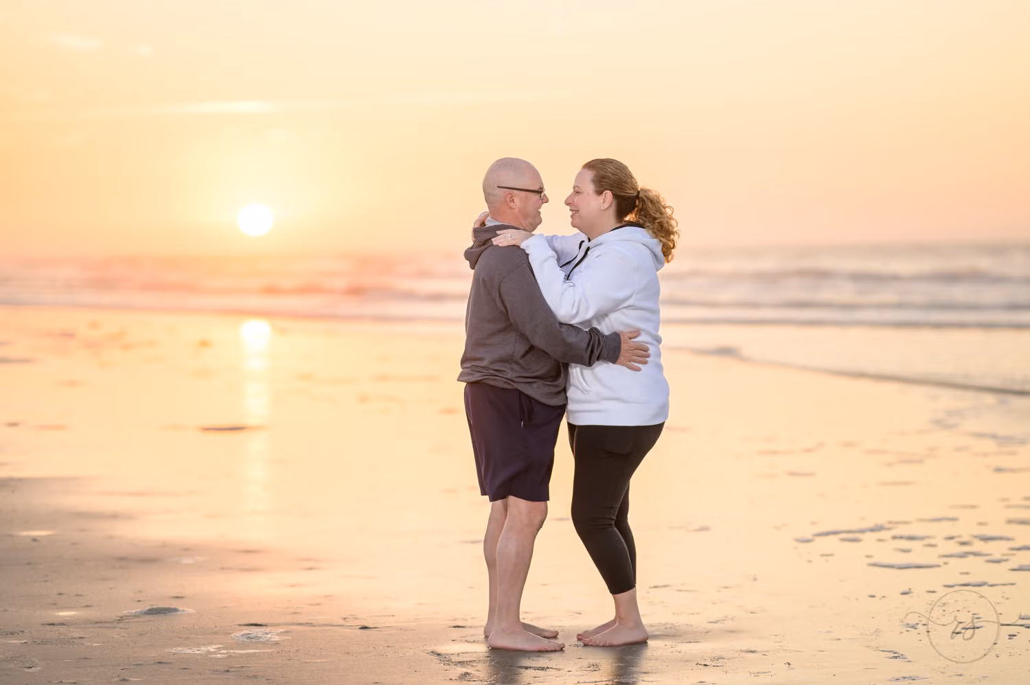 Newly engaged couple hugging on the beach as the sun rises over the ocean behind them in Sunset Beach