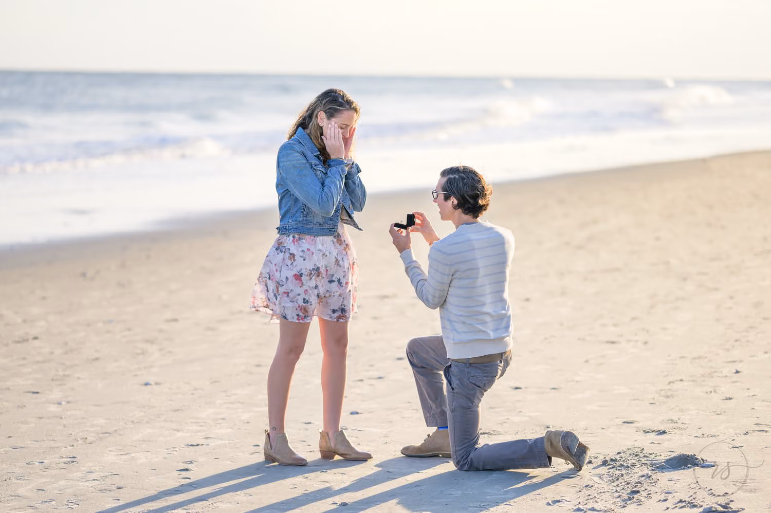 Man down on one knee proposing on the sand as she covers her face in surprise at the Marriott in Myrtle Beach