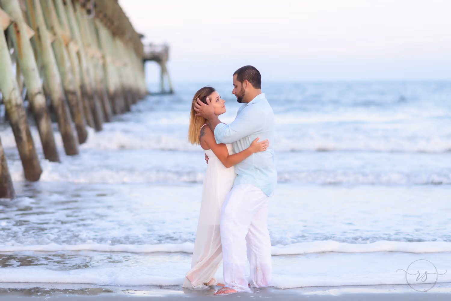 Couple embracing in the shallow surf beside the pier at sunset at Myrtle Beach State Park