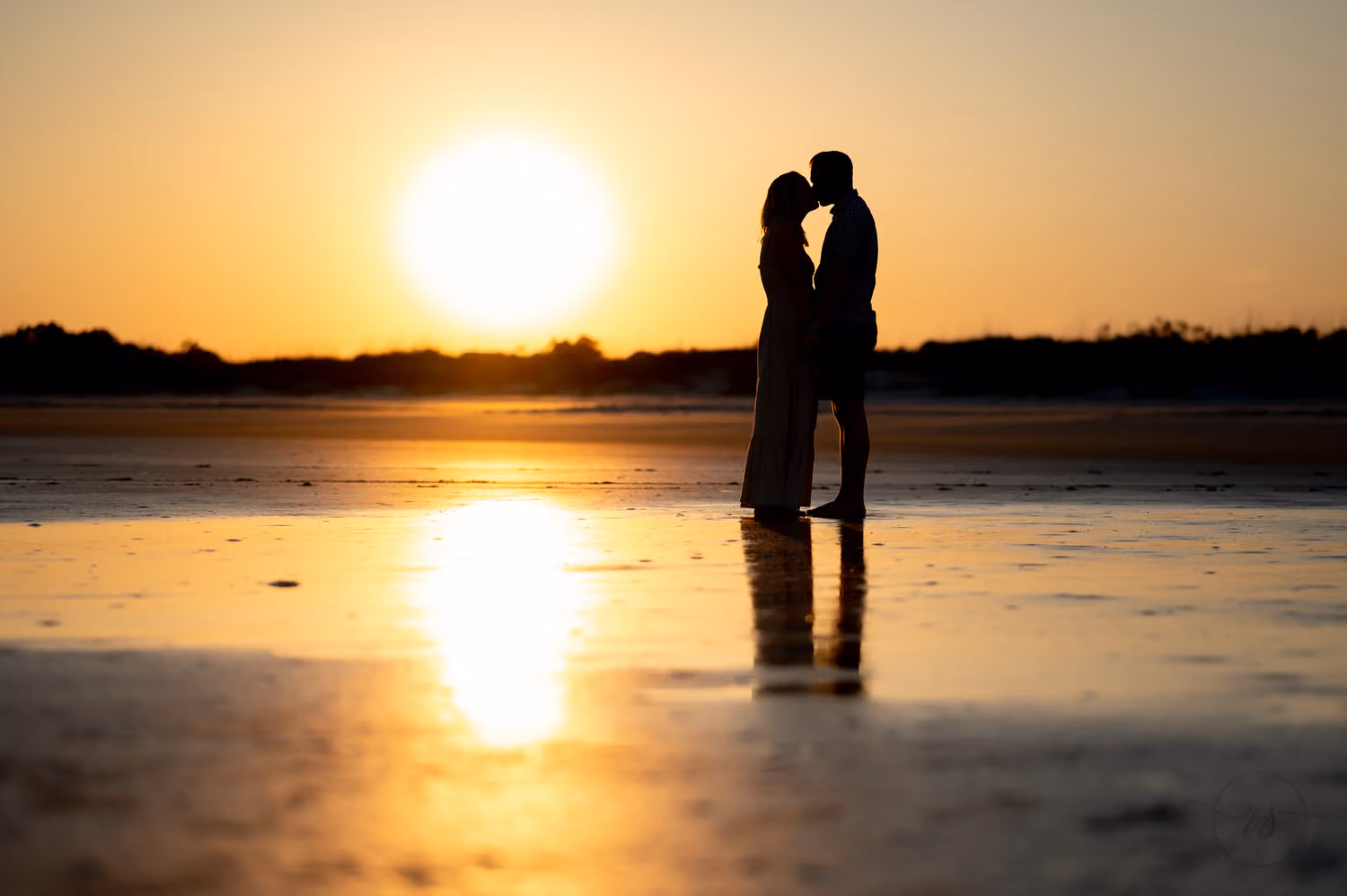 Silhouette of a just engaged couple kissing as the setting sun reflects on the wet sand at Inlet Point Plantation