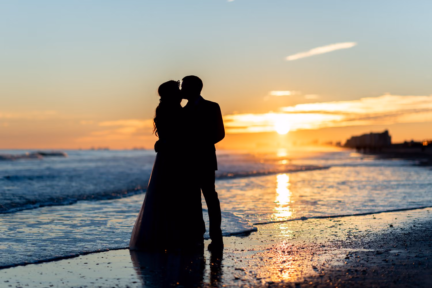 Silhouette of the bride and groom kissing at the water's edge as the sun sets over the ocean at Cherry Grove