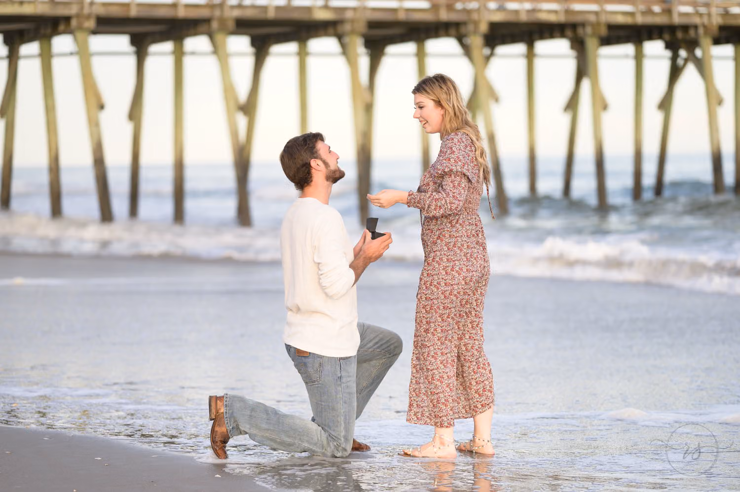 Man kneeling with a ring as she smiles in front of the fishing pier at Myrtle Beach State Park