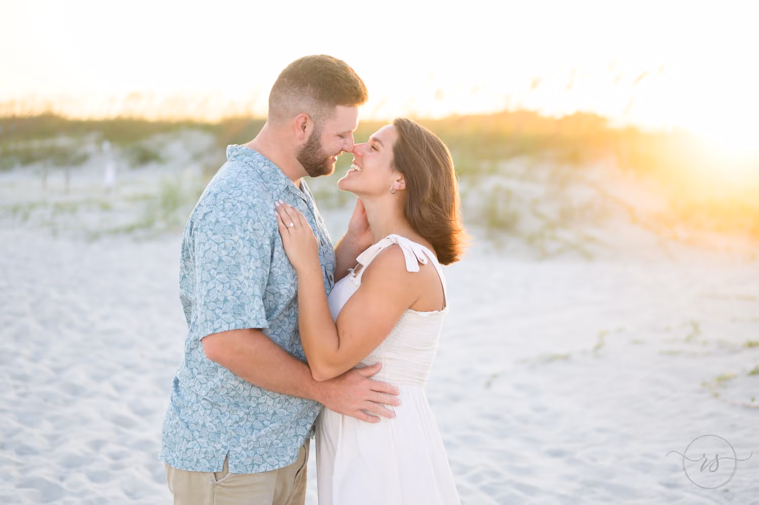 Couple touching noses as the setting sun glows behind the dunes at Huntington Beach State Park